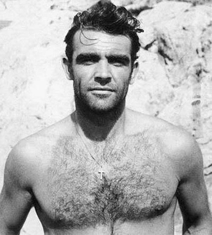 a shirtless man with no shirt standing in front of a rock wall and looking at the camera