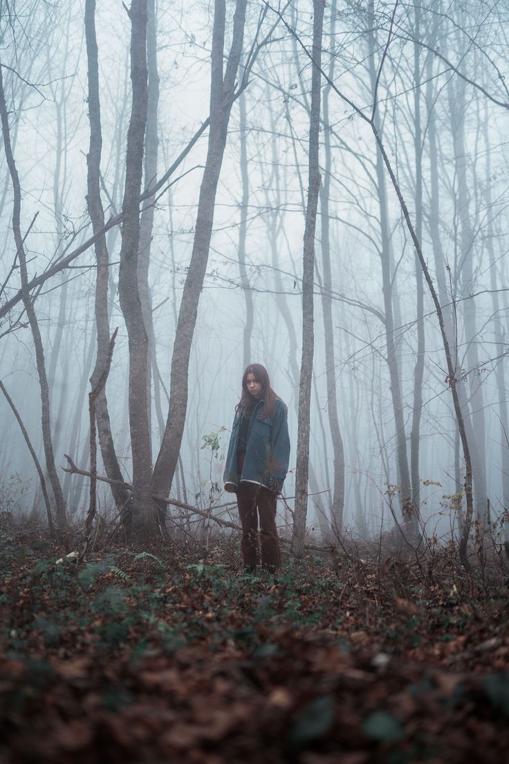 a woman standing in the middle of a forest on a foggy day with trees