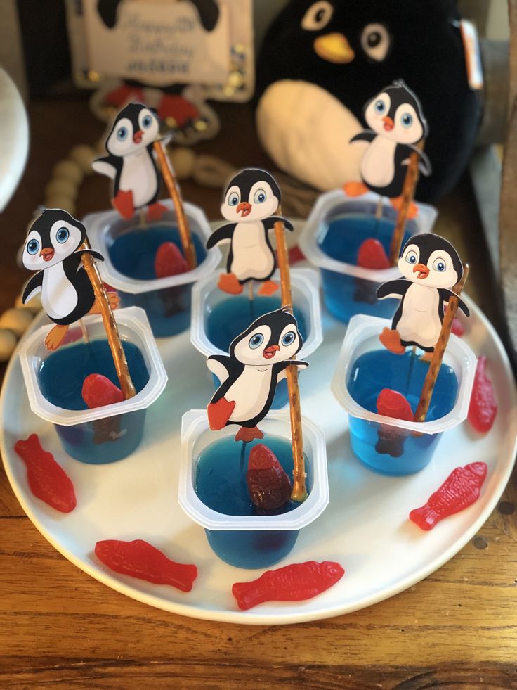 there are many small cups with little penguins in them on the plate and one is holding a stick