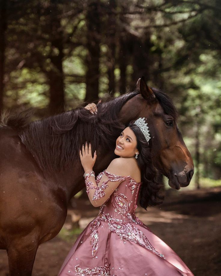 a woman in a pink dress standing next to a brown horse and posing for the camera