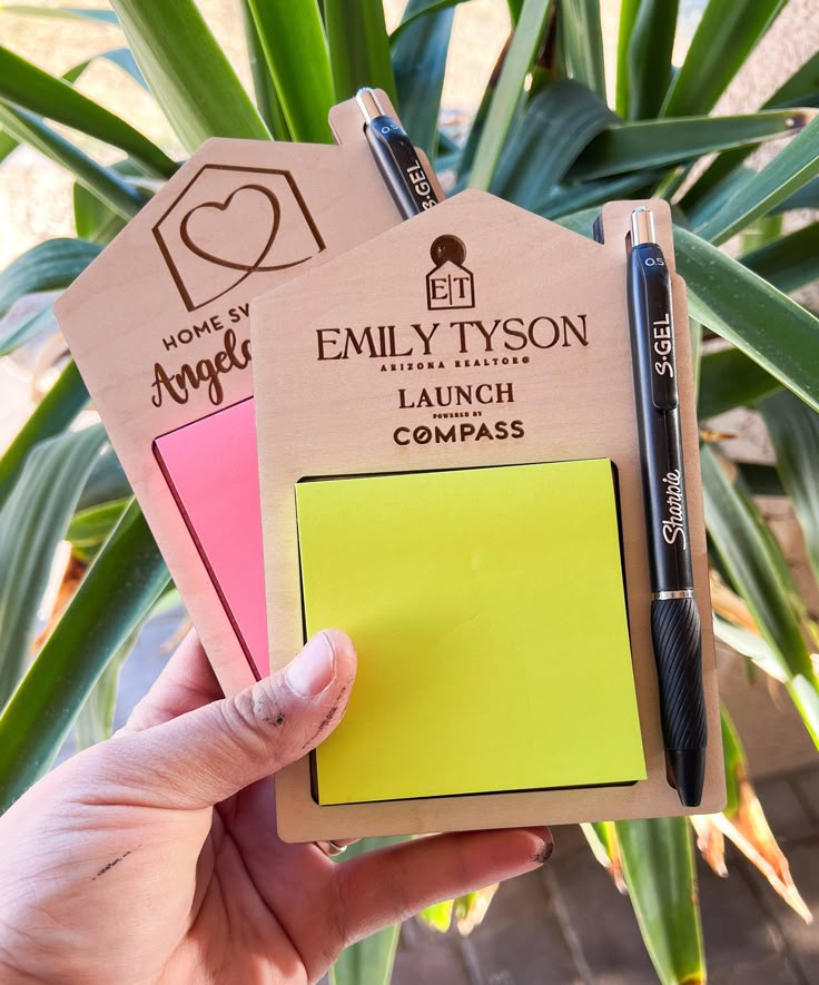 a person holding two sticky notes and a pen in front of a potted plant