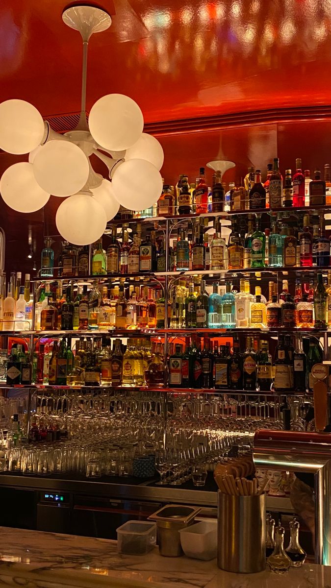 a bar with lots of bottles and glasses on the shelves, lights hanging from the ceiling