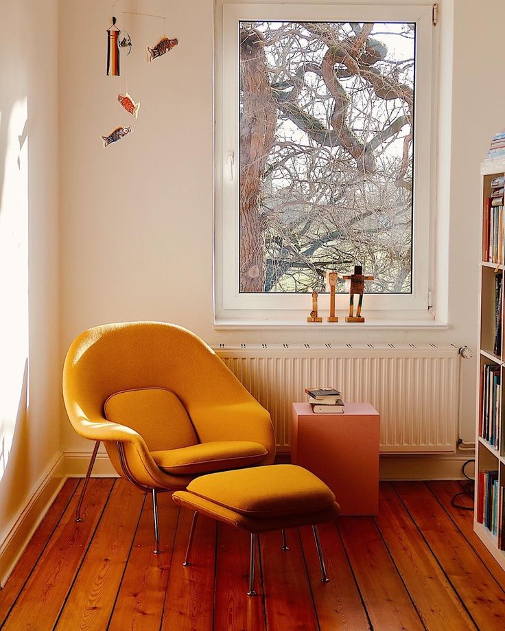 a yellow chair sitting in front of a window next to a book shelf