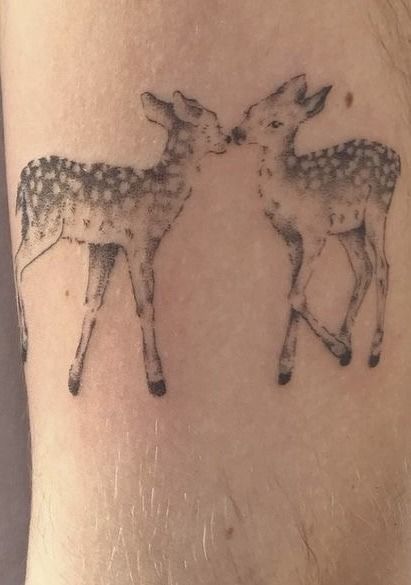 a couple of deer standing next to each other on a person's leg with tattoos