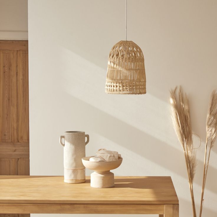 a wooden table topped with white vases next to a light brown lamp hanging from the ceiling