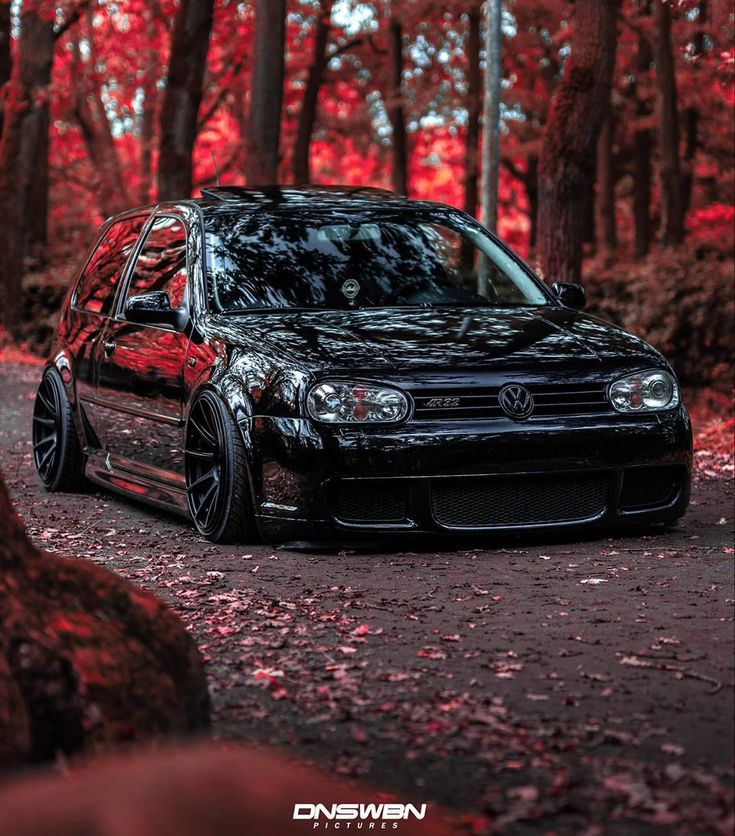 a black car parked on the side of a road in front of trees with red leaves