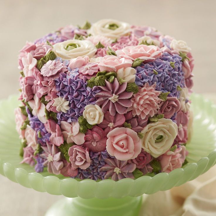 a cake decorated with pink, purple and white flowers on a green plate sitting on a table