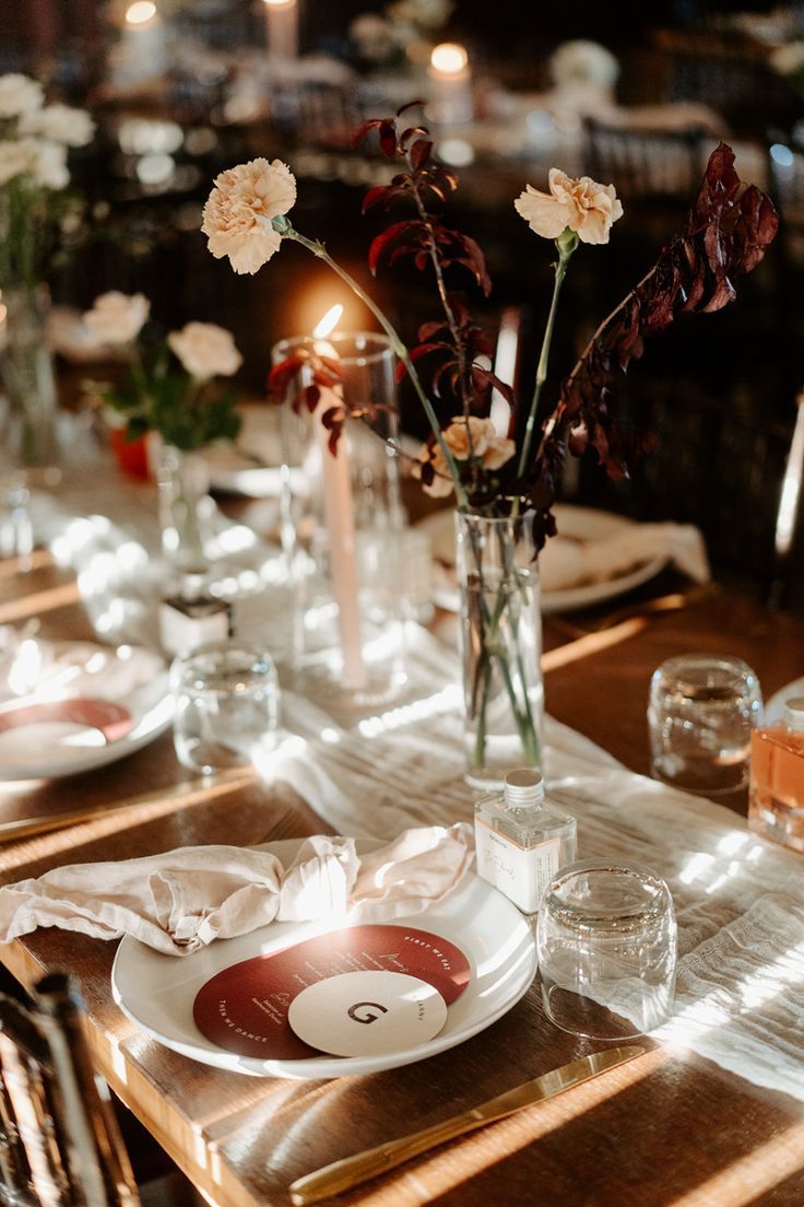 the table is set with plates, glasses and flowers in vases on top of them