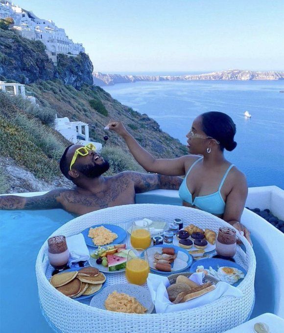 a man and woman sitting in a pool with food on the table next to them