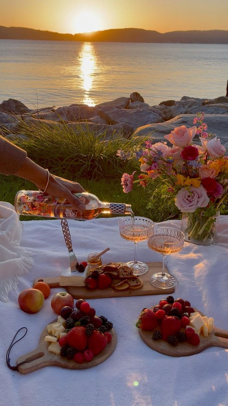 a table topped with fruit and cheese on top of a white cloth covered table next to the ocean