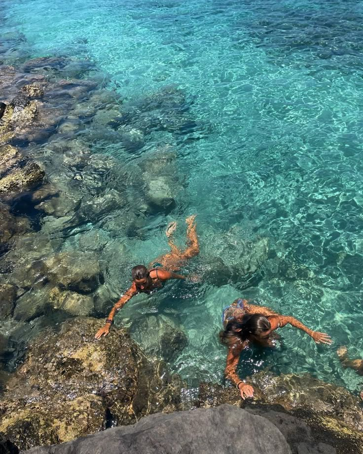 two people are swimming in the clear blue water