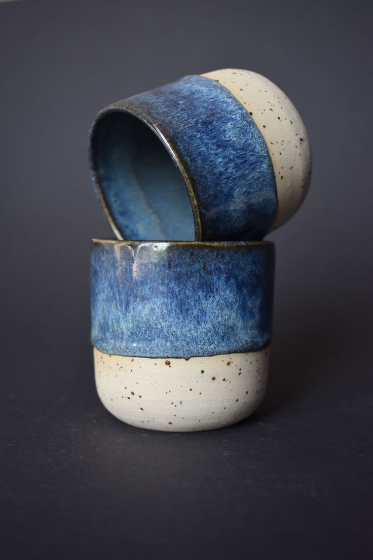 two blue and white ceramic containers sitting on top of a black surface with speckles