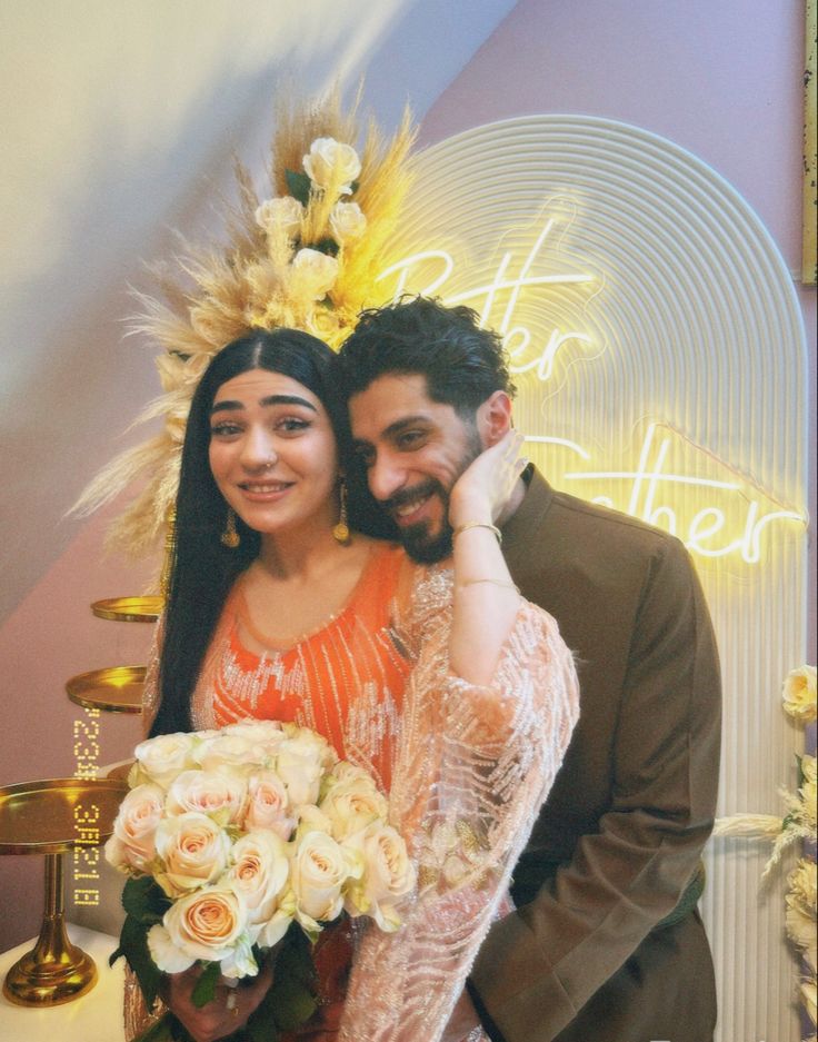 a man and woman standing next to each other in front of a sign with flowers on it