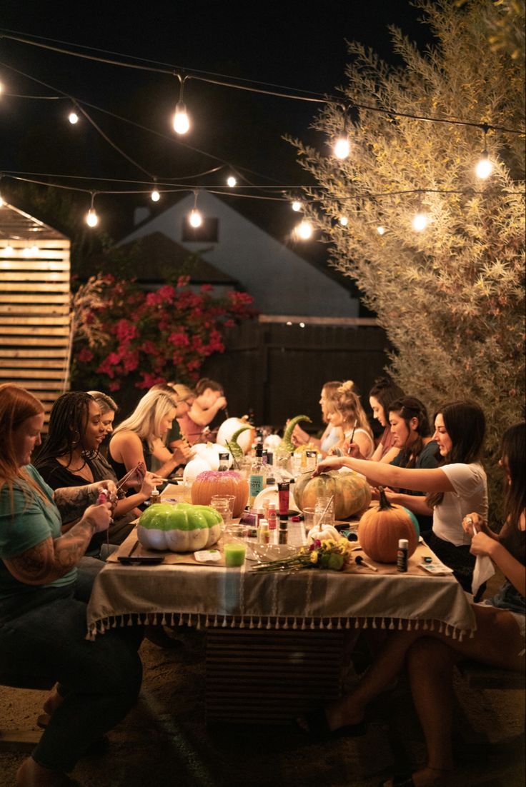 a group of women sitting around a table with food and drinks on it at night