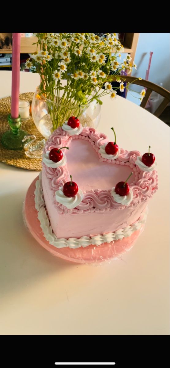 a pink heart shaped cake sitting on top of a table next to a vase with flowers