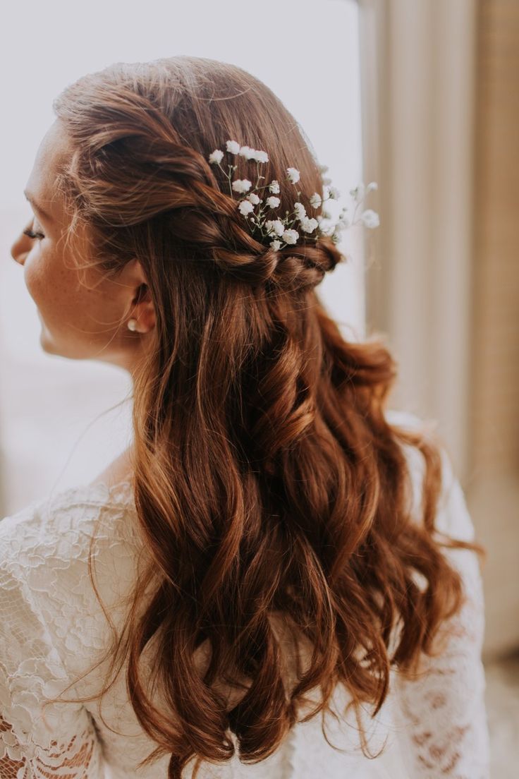 a woman with long brown hair wearing a white dress and flowers in her hair is looking out the window