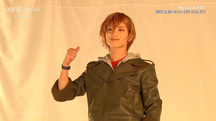 a woman in a leather jacket is giving the peace sign with her right hand while standing against a white backdrop