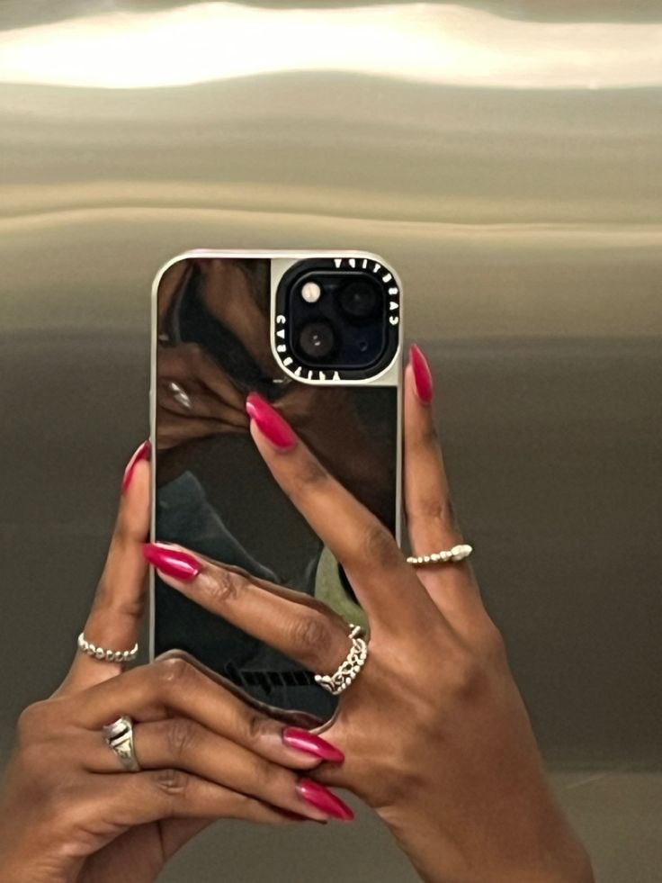 a woman taking a selfie with her phone in front of an elevator door while wearing pink nail polish