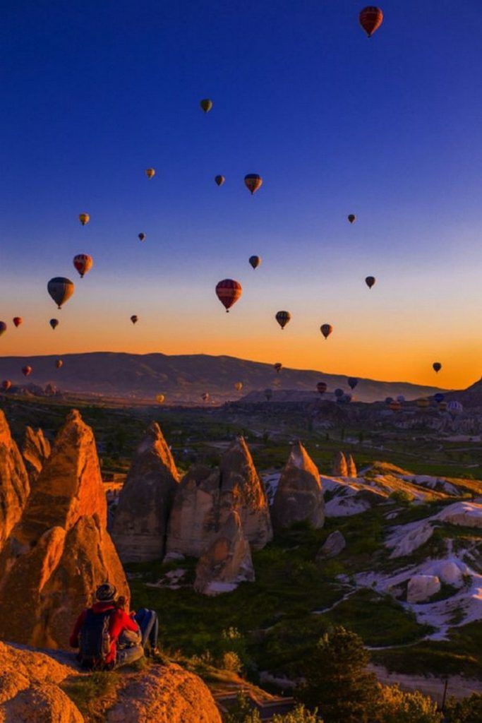 many hot air balloons are flying in the sky above some rocks and trees at sunset