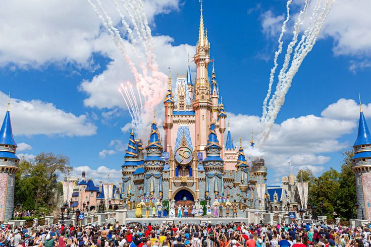 people are watching fireworks in front of the castle at disneyland world with blue sky and clouds