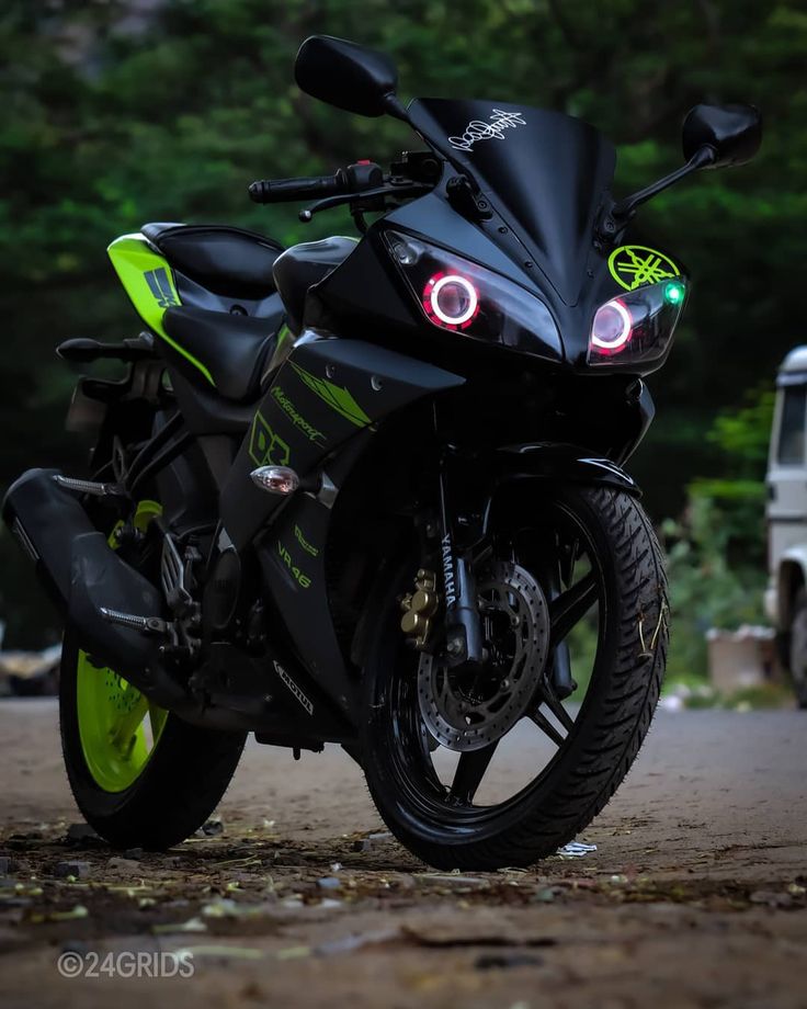 the motorcycle is parked on the side of the road with its lights turned on and there are trees in the background