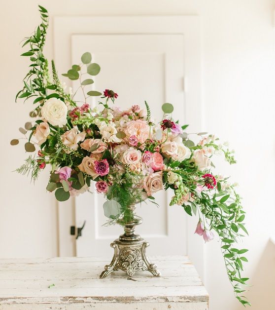 a vase filled with pink and white flowers on top of a wooden table next to a door