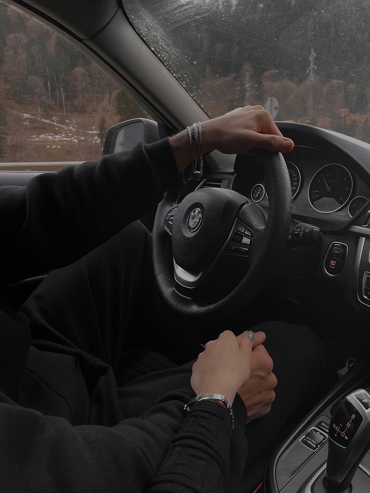 a person driving a car in the rain with their hands on the steering wheel and dashboard