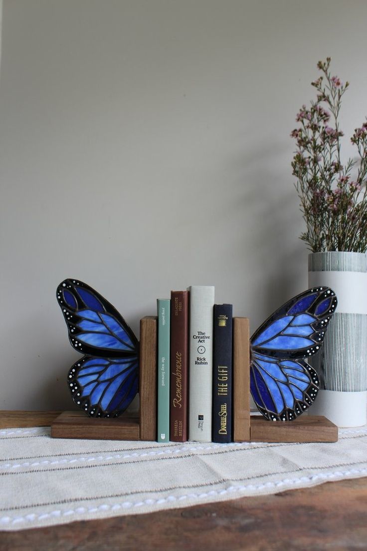 a blue butterfly sitting on top of books next to a vase with flowers in it