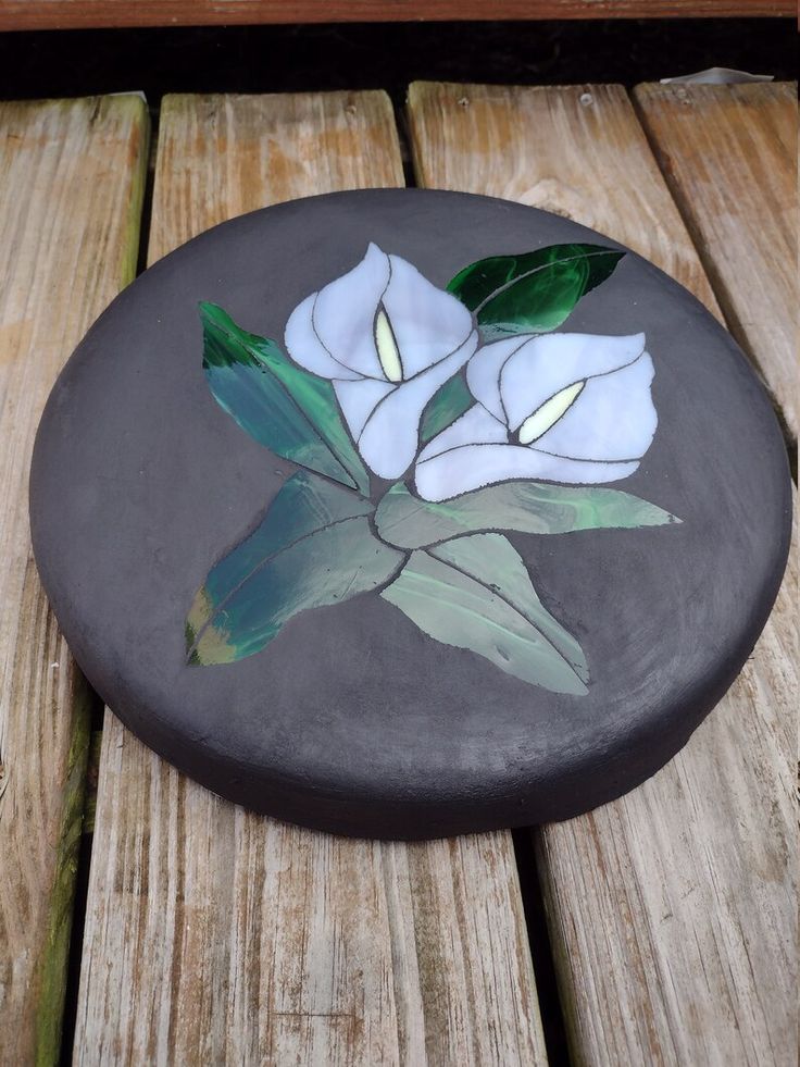 a painted rock with flowers on it sitting on a wooden table next to a bench