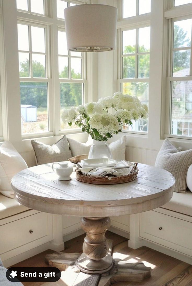 a table with flowers in a vase on top of it next to some pillows and windows