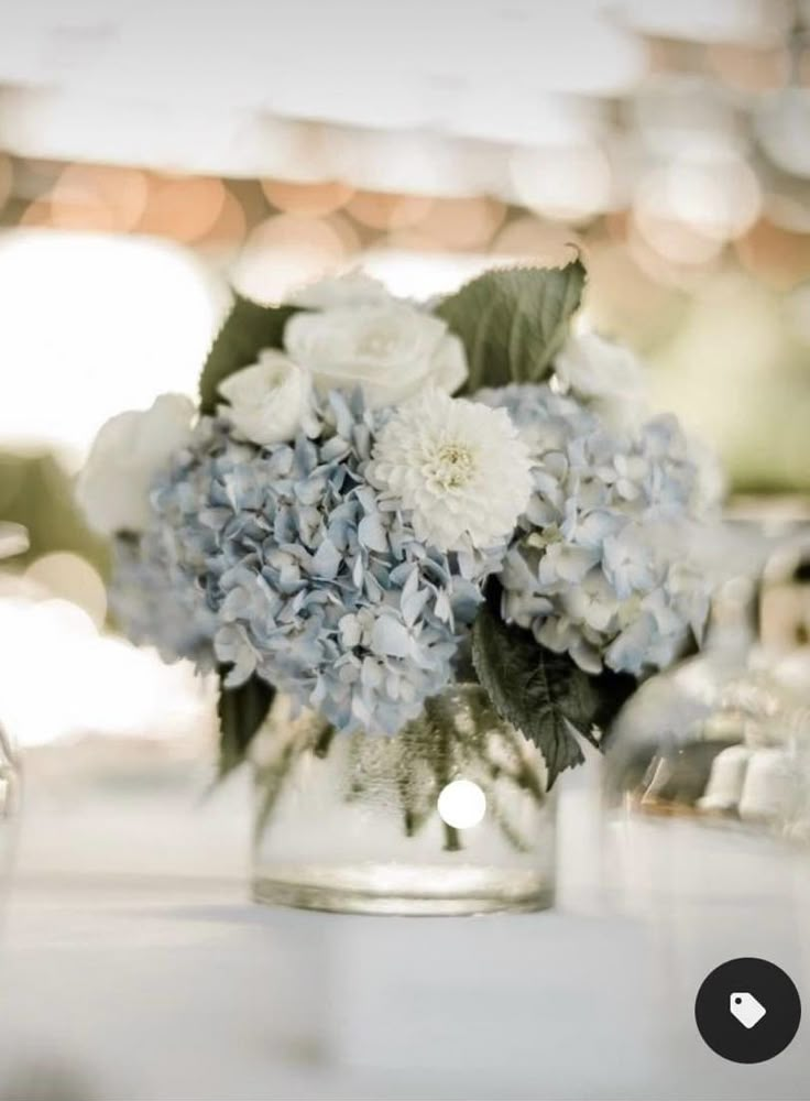 a glass vase filled with blue and white flowers on top of a table next to glasses