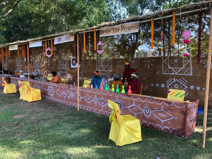 a long table with decorations on it in the middle of some grass and people standing around