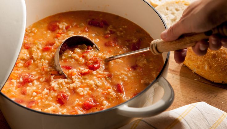 a person stirring soup in a pot with a ladle and bread on the side