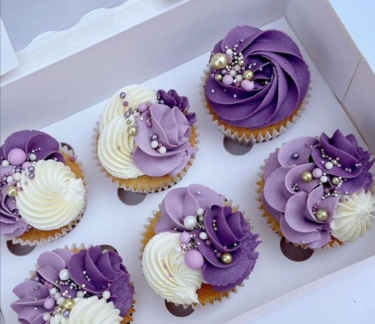 six cupcakes in a box decorated with purple and white icing, pearls and flowers