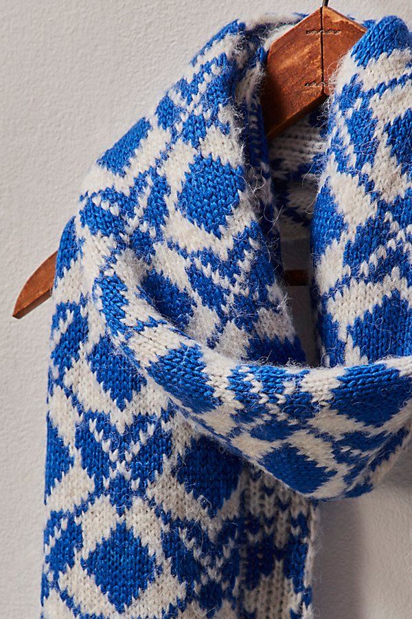 a blue and white knitted scarf hanging on a wooden hanger next to a wall