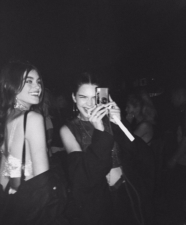 black and white photograph of two women taking pictures with their cell phones at a party