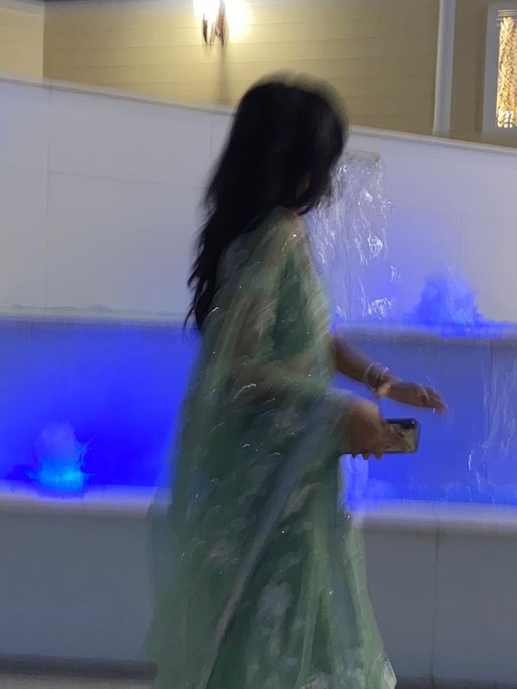 a woman in a green sari walking past a fountain with blue lights on it