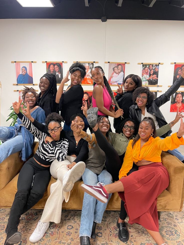 a group of women sitting on top of a couch in front of pictures hanging on the wall