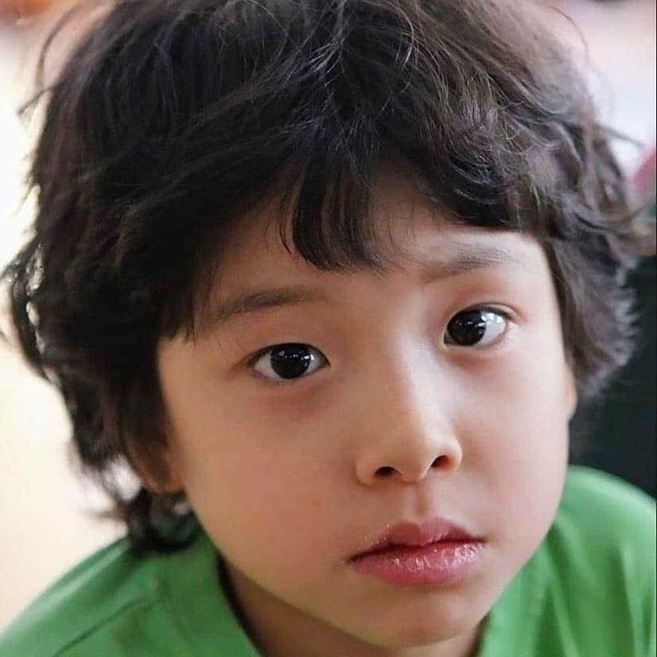 a close up of a young child wearing a green shirt and looking at the camera