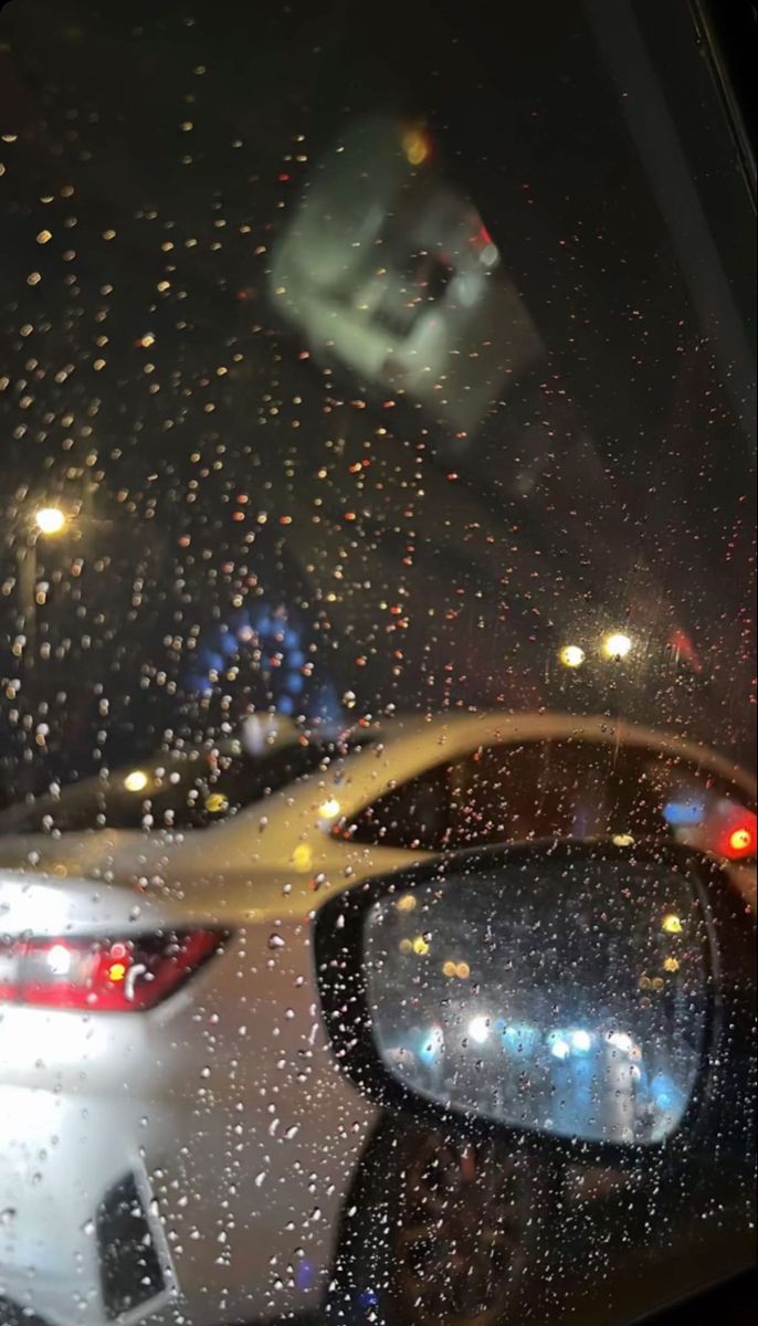 rain is falling on the windshield of a car as it drives down a street at night