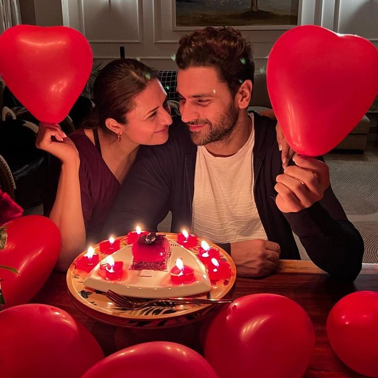 a man and woman sitting in front of a heart shaped cake with candles on it