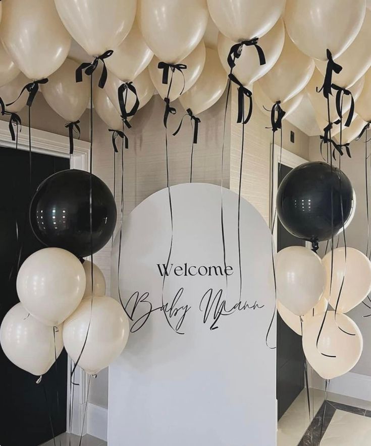 white and black balloons are hanging from the ceiling in front of a sign that reads welcome baby mama