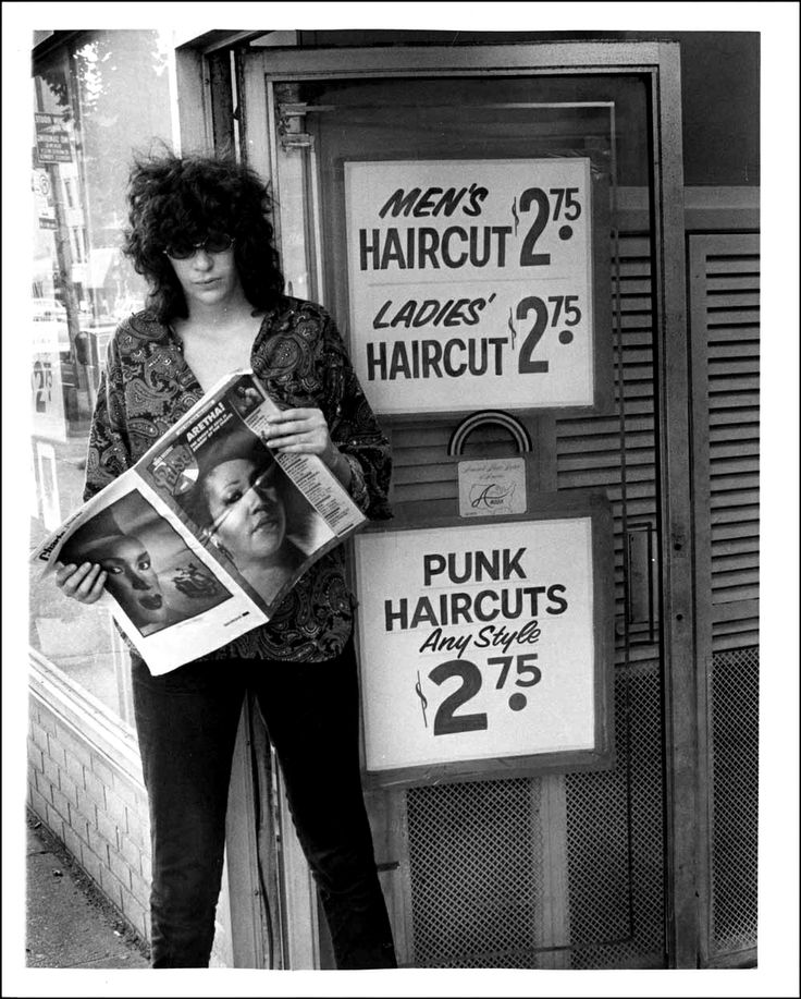 a woman standing in front of a hair salon holding a newspaper and looking at it