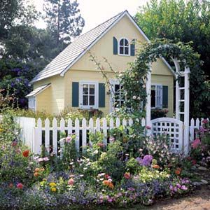 a yellow house surrounded by flowers and greenery