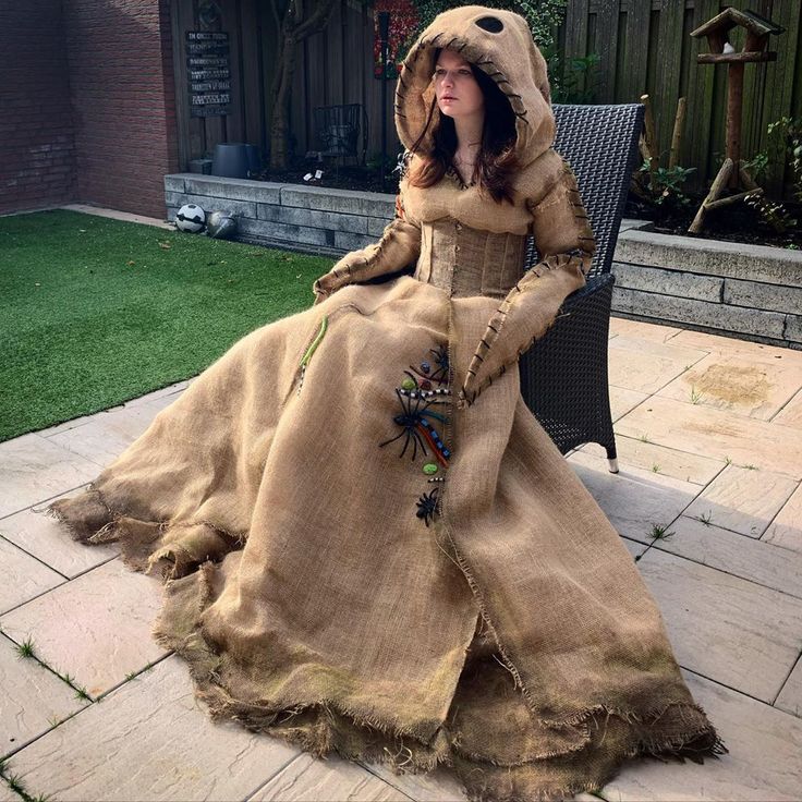 a woman in a long dress sitting on a patio chair wearing a hood and gloves