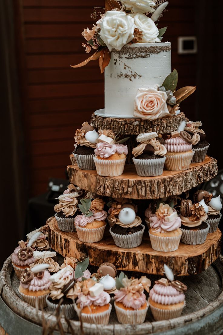 a three tiered cake with cupcakes and flowers on top