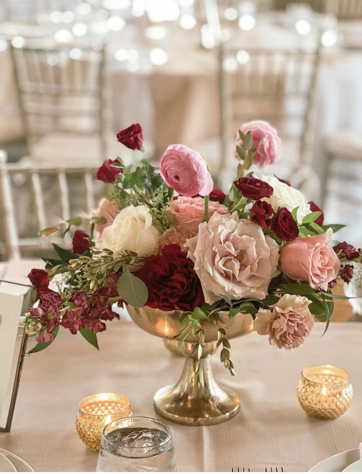 a vase filled with pink and red flowers on top of a table next to candles