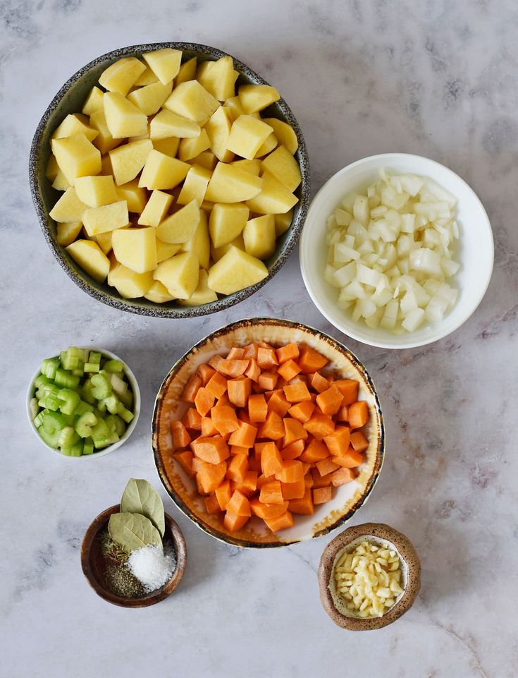 bowls filled with chopped up vegetables on top of a white marble counter next to small bowls full of diced potatoes