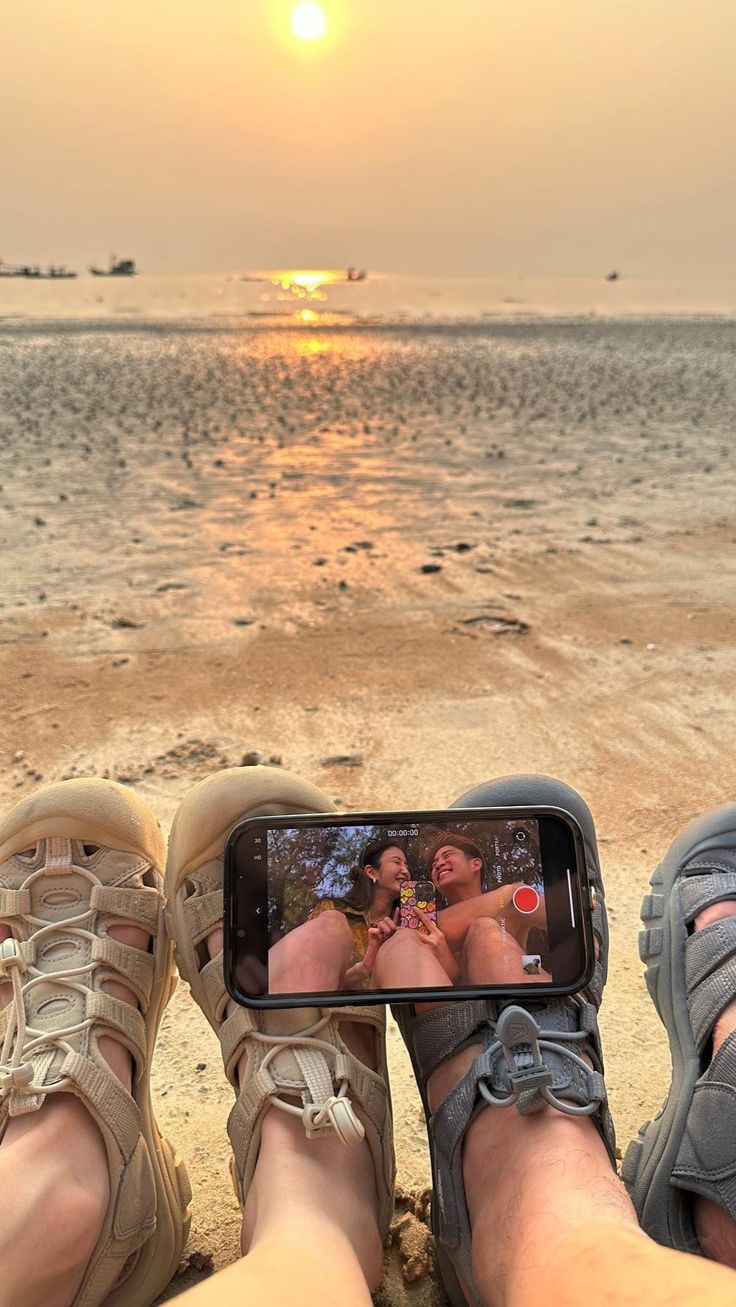 two people sitting on the beach with their feet propped up in front of an iphone