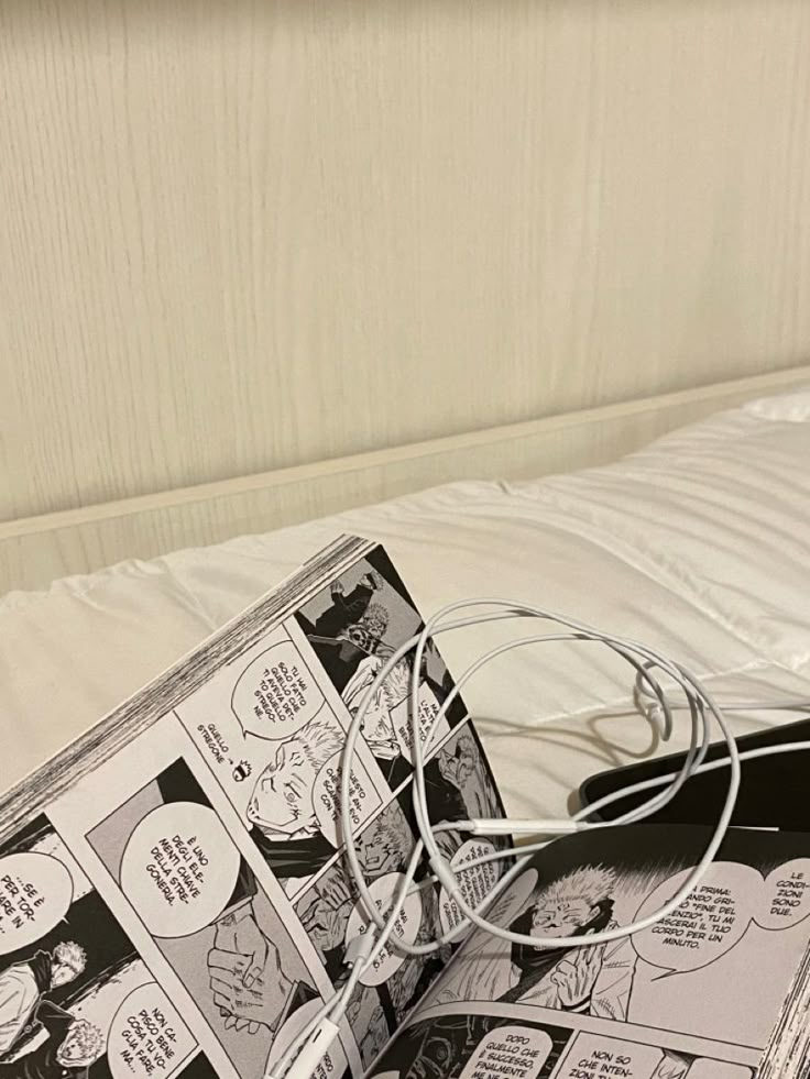 an open comic book sitting on top of a bed with headphones attached to it